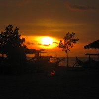 Just down from Kuta Beach, Bali. One of the last sunsets of 2009, I love the colours dancing off the water behind the boats. The fire on the beach was built by a local as his friends gathered near the hut to the left for some barbeque and drinks.